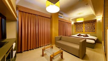 A hotel room with a bed, sofa, glass coffee table, curtains, and a television.