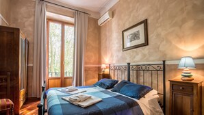 Un dormitorio con una colcha a cuadros, una mesita de noche de madera con una lámpara y una ventana con cortinas.