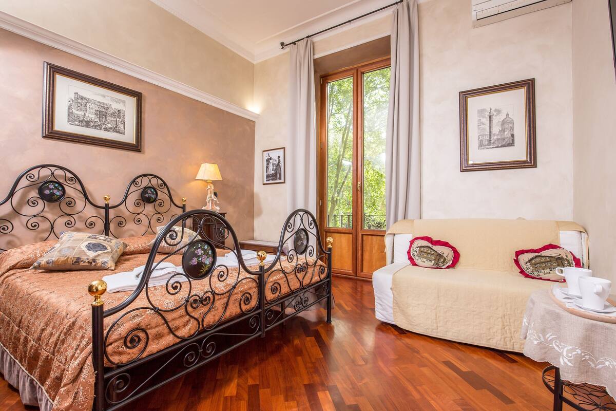 A bedroom with a bed, a sofa, a table with a cup, and two framed pictures on the wall.