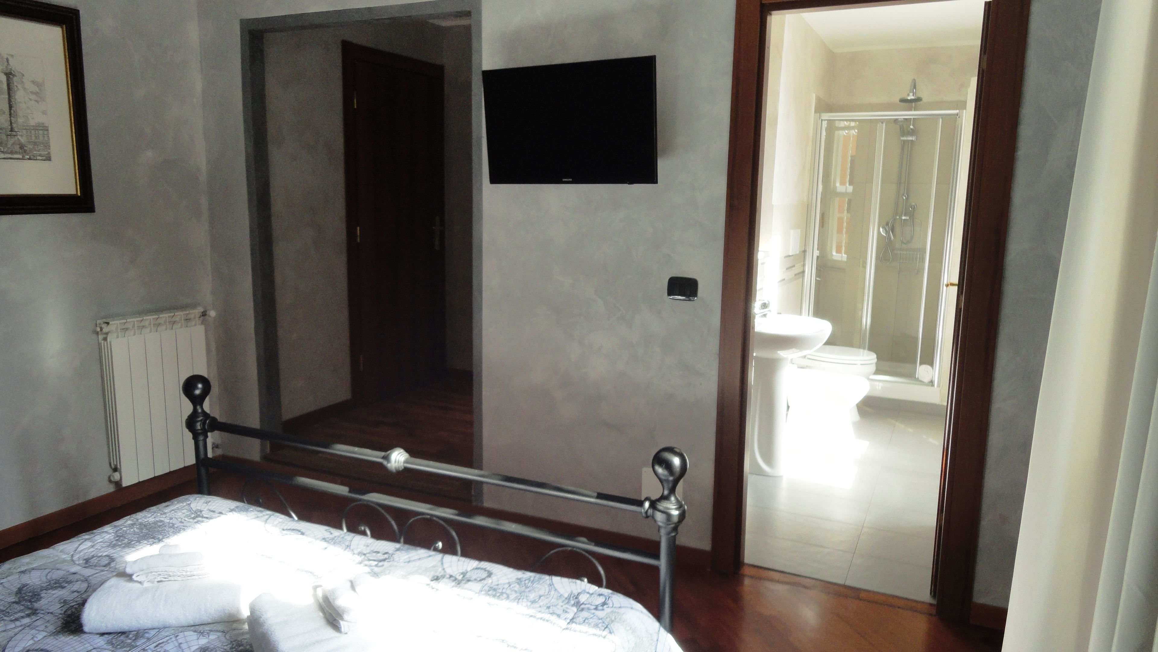 A bedroom with a bed, a bedside table, a mirror, and a door leading to a bathroom with a shower and toilet.