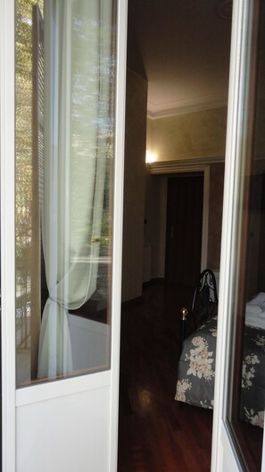 Un dormitorio con cama, ventana con cortinas y puerta que da a otra habitación.