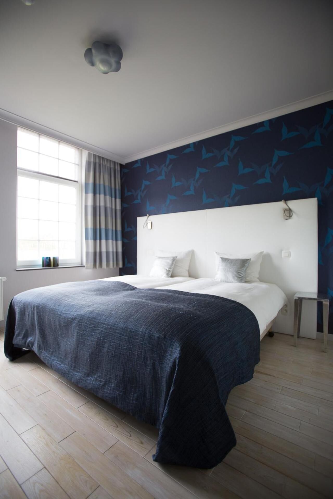 A modern bedroom with a large bed, a window with curtains, and a wall with a leaf pattern.