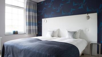 A modern bedroom with a large bed, a window with curtains, and a wall with a leaf pattern.