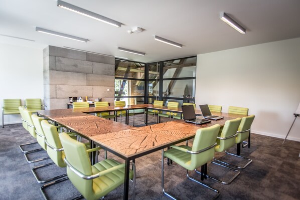 Un salón de conferencias con una mesa grande, sillas verdes y una computadora portátil sobre la mesa.