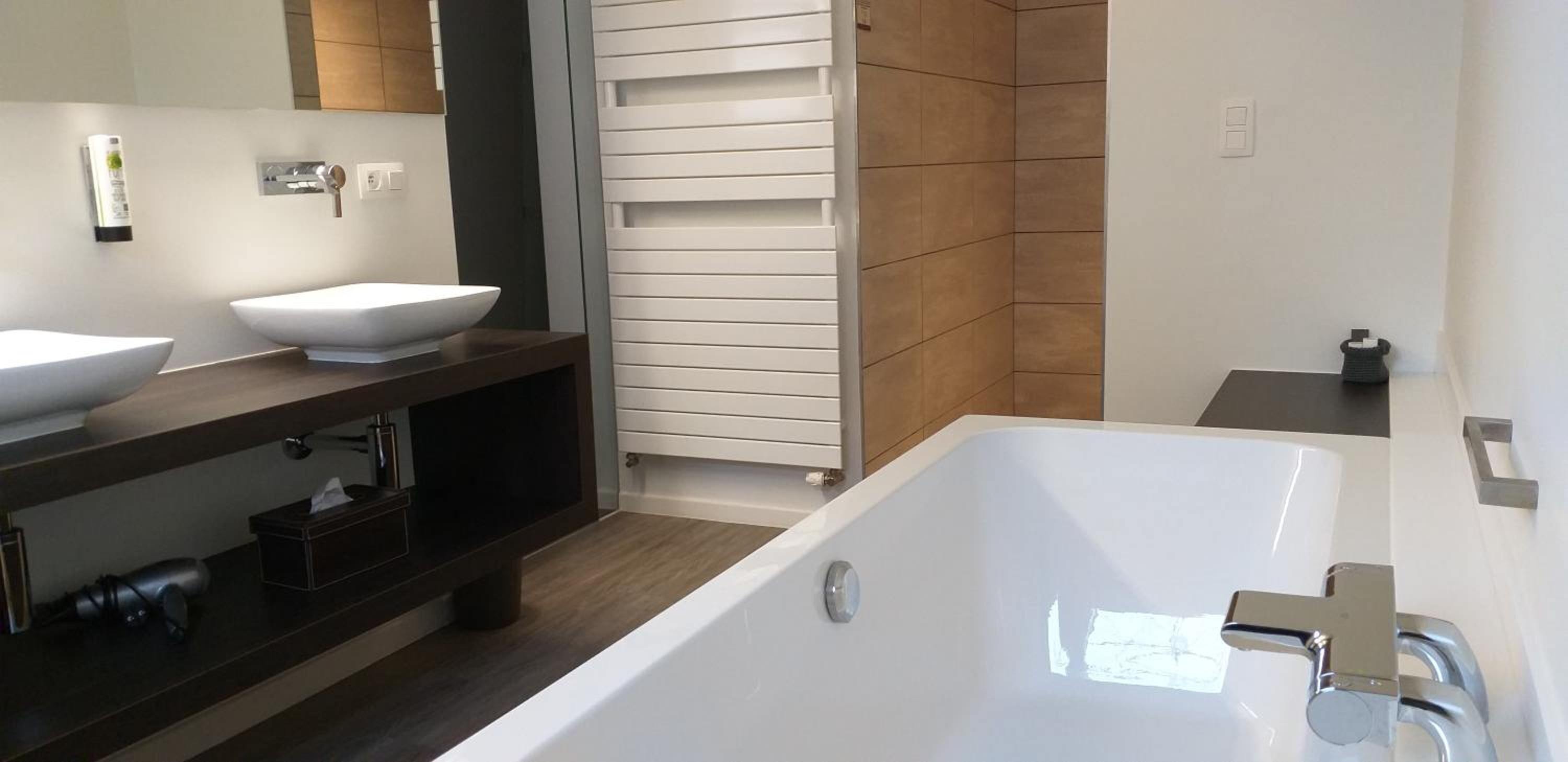 A modern bathroom with a large bathtub, two white vessel sinks, a dark wooden vanity, and a towel rack.