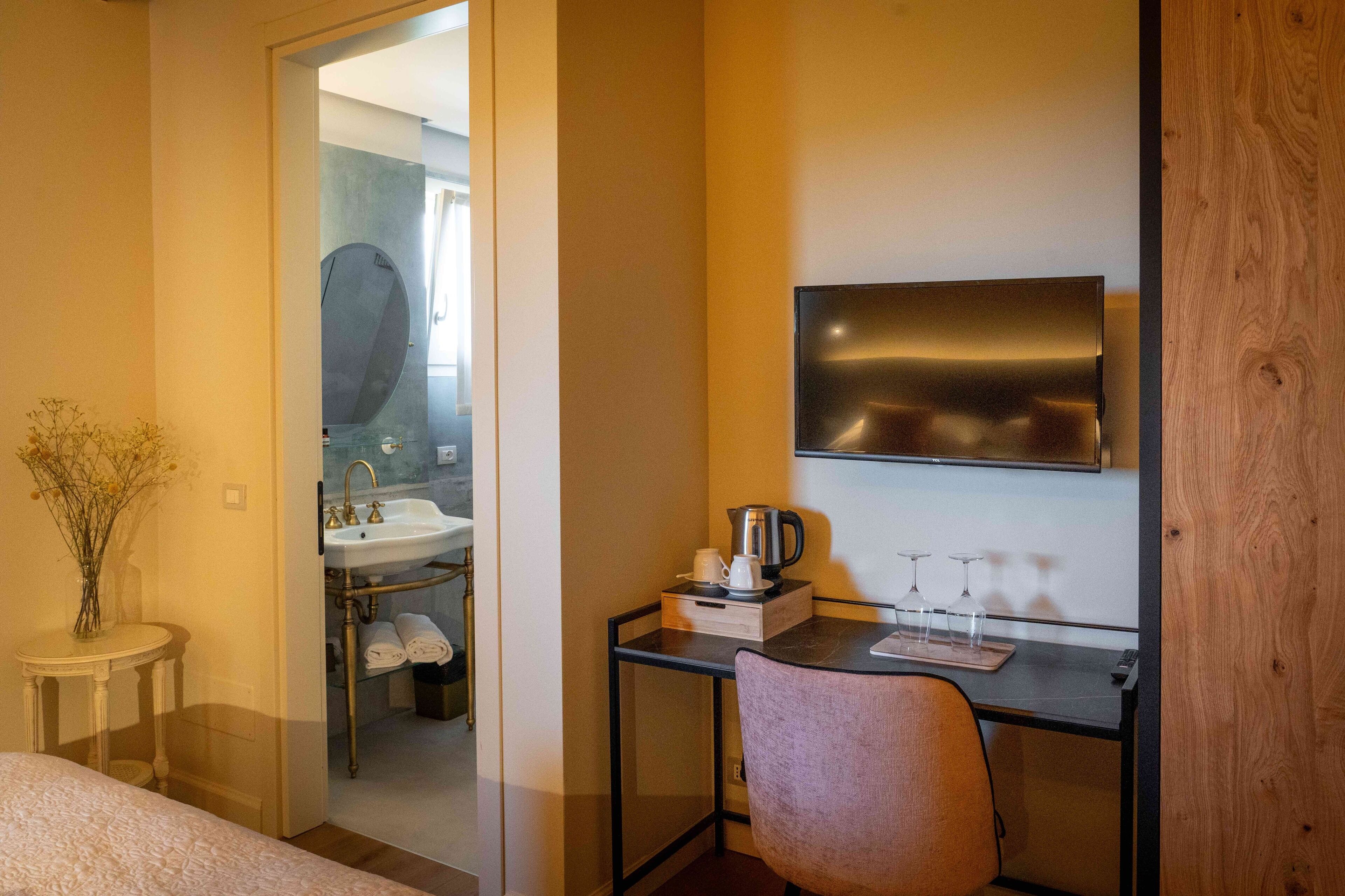 A hotel room with a bed, a desk with a chair, a mirror, a sink, and a television.