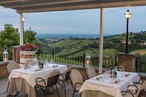 An outdoor dining area with tables set for two, overlooking a scenic valley. - Agriturismo Acetaia Sereni (Marano sul Panaro)