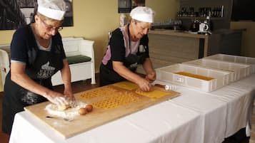 Two individuals preparing food on a table with a cutting board and white plastic containers.