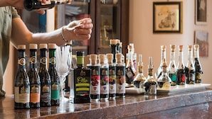 Eine Person gießt ein Getränk aus einer Flasche in ein Glas. Auf der Theke stehen mehrere Flaschen mit verschiedenen alkoholischen Getränken.