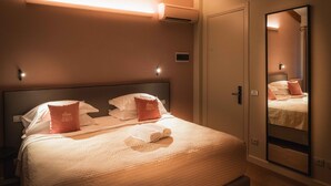 Ein ordentlich bezogenes Bett mit Kissen, einem Nachttisch und einem Spiegel an der Wand.