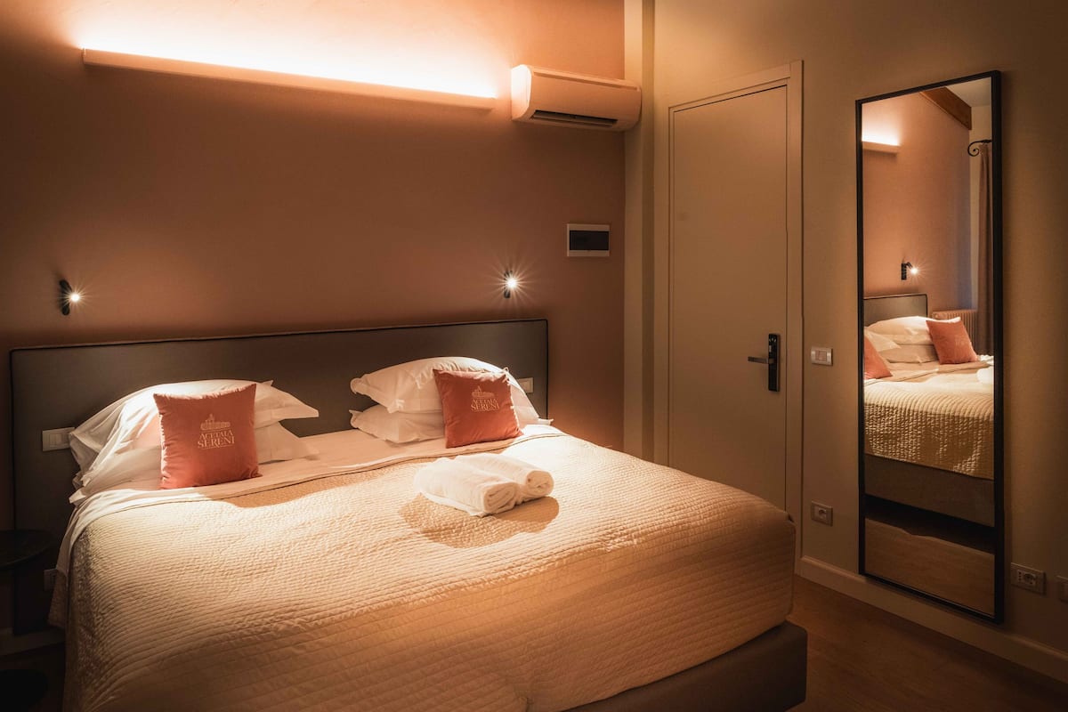A neatly made bed with pillows, a bedside table, and a mirror on the wall.