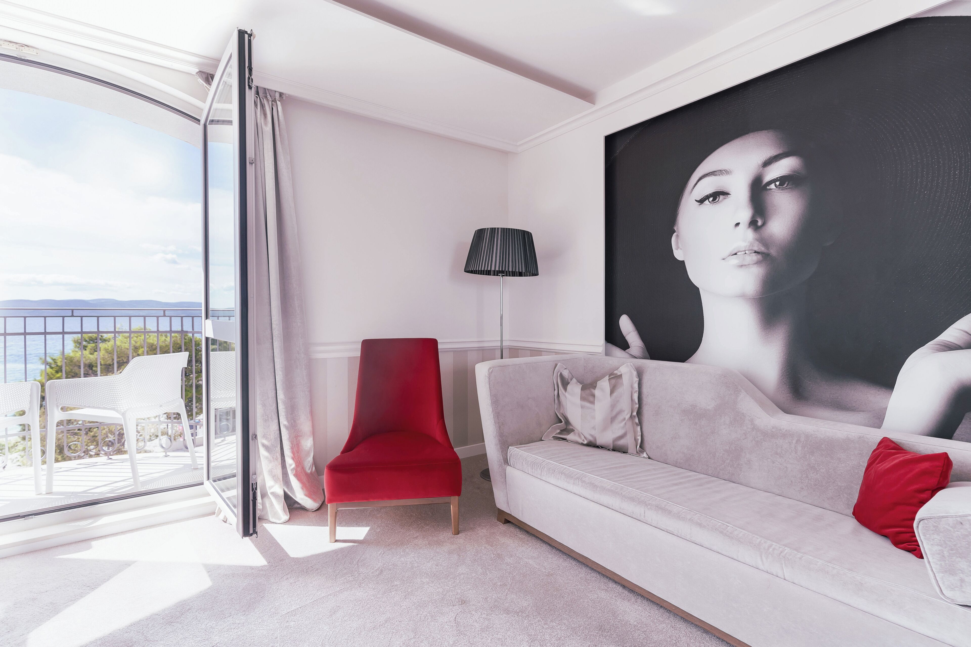 A modern living room with a red chair, a grey sofa, and a large painting on the wall.