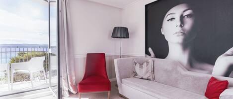 A modern living room with a red chair, a grey sofa, and a large painting on the wall.