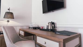 Habitación de hotel con un escritorio de madera, una silla, un televisor de pantalla plana, una lámpara y una cafetera.