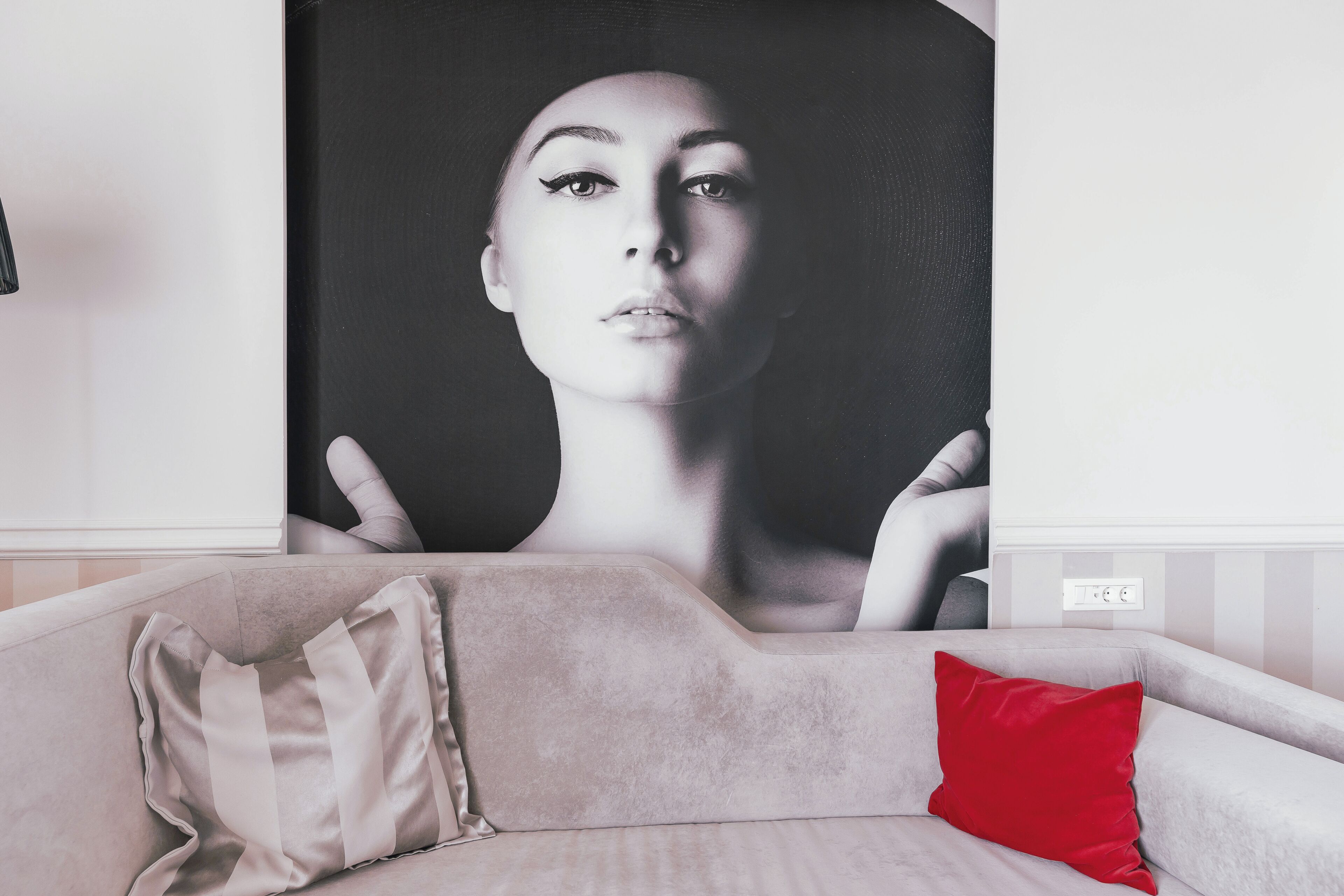 Una sala de estar con un sofá, un cojín rojo y un gran retrato blanco y negro en la pared.