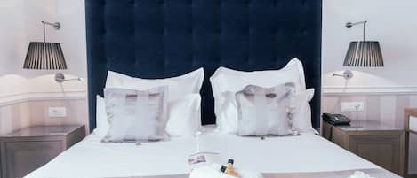A neatly made bed with white linens, two bedside lamps, and a rolled towel with a bottle on it.