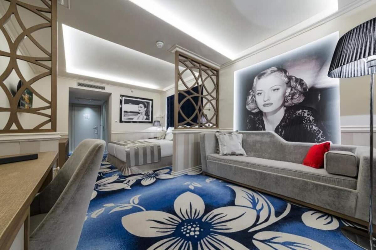 A modern living room with a sofa, a dining area, and a large floral-patterned carpet.