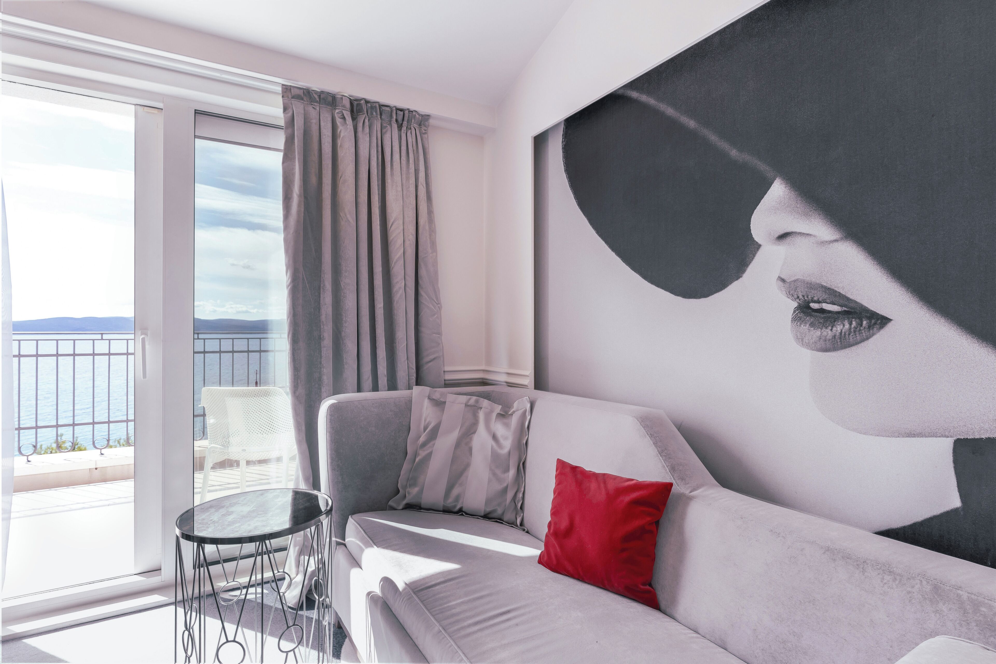A modern room with a balcony, a sofa, a red pillow, and a large abstract painting.