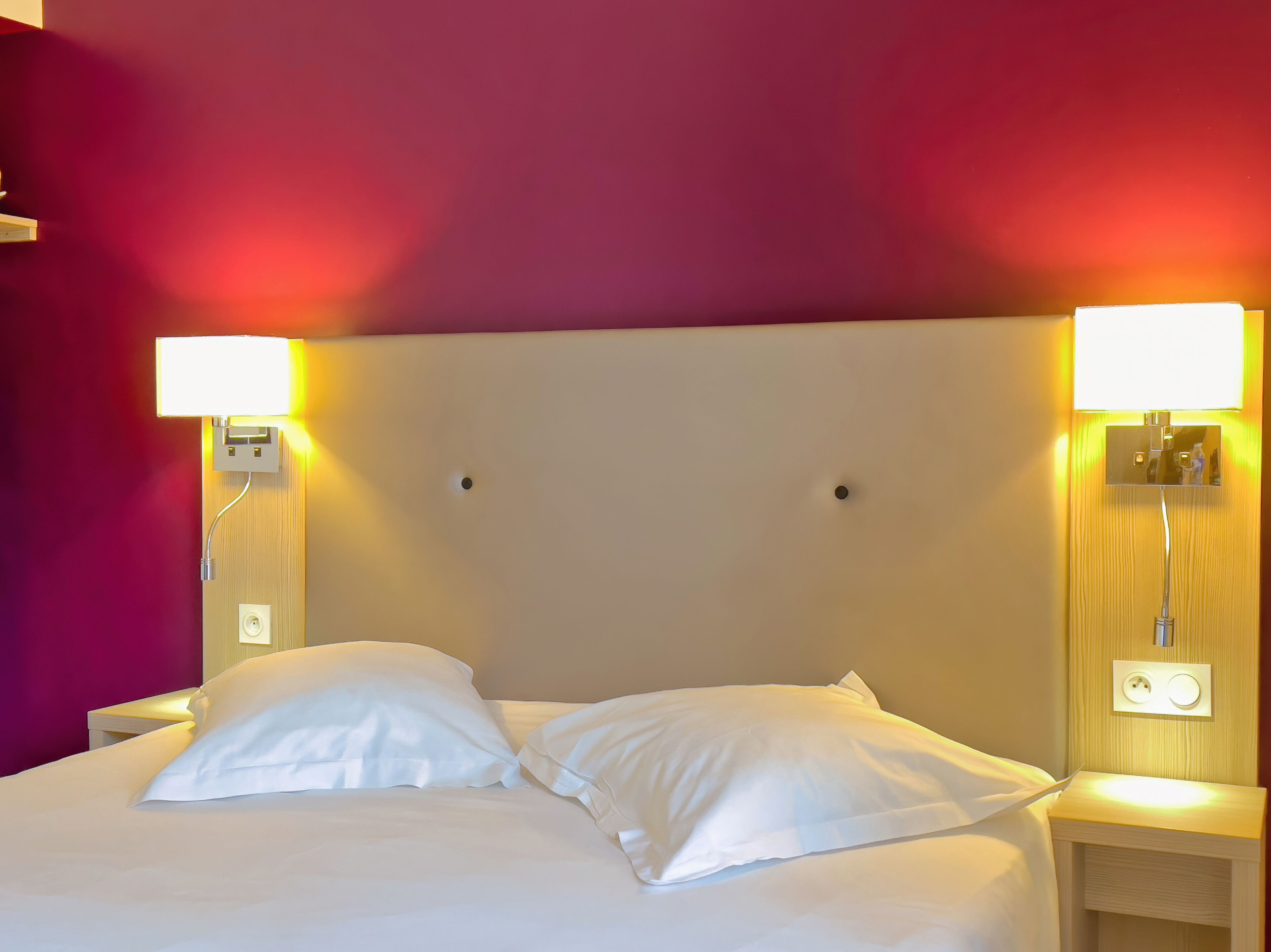 A hotel room with a bed, two bedside lamps, and a nightstand.