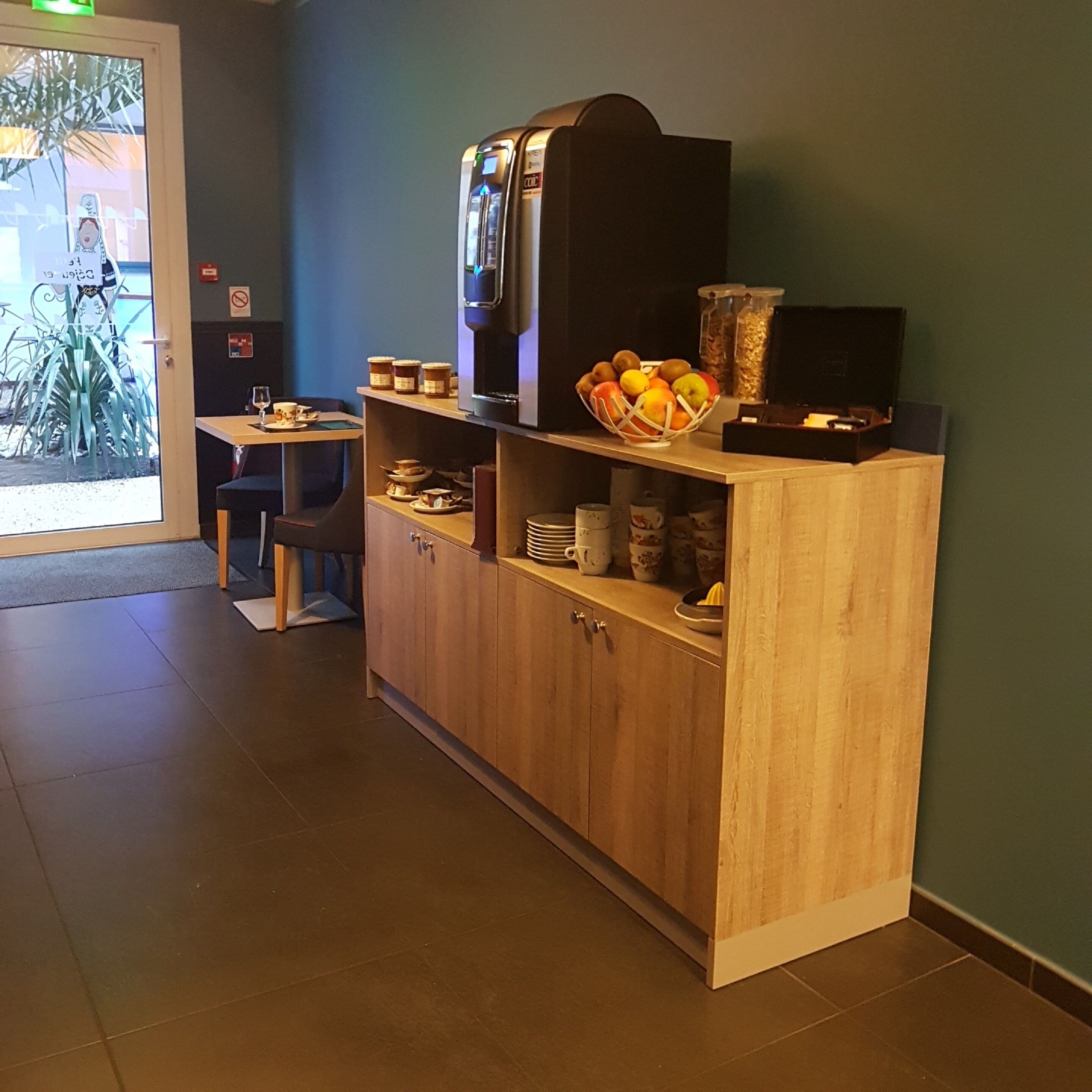 Un espace d’accueil avec un comptoir en bois, une machine à café et un panier de fruits.
