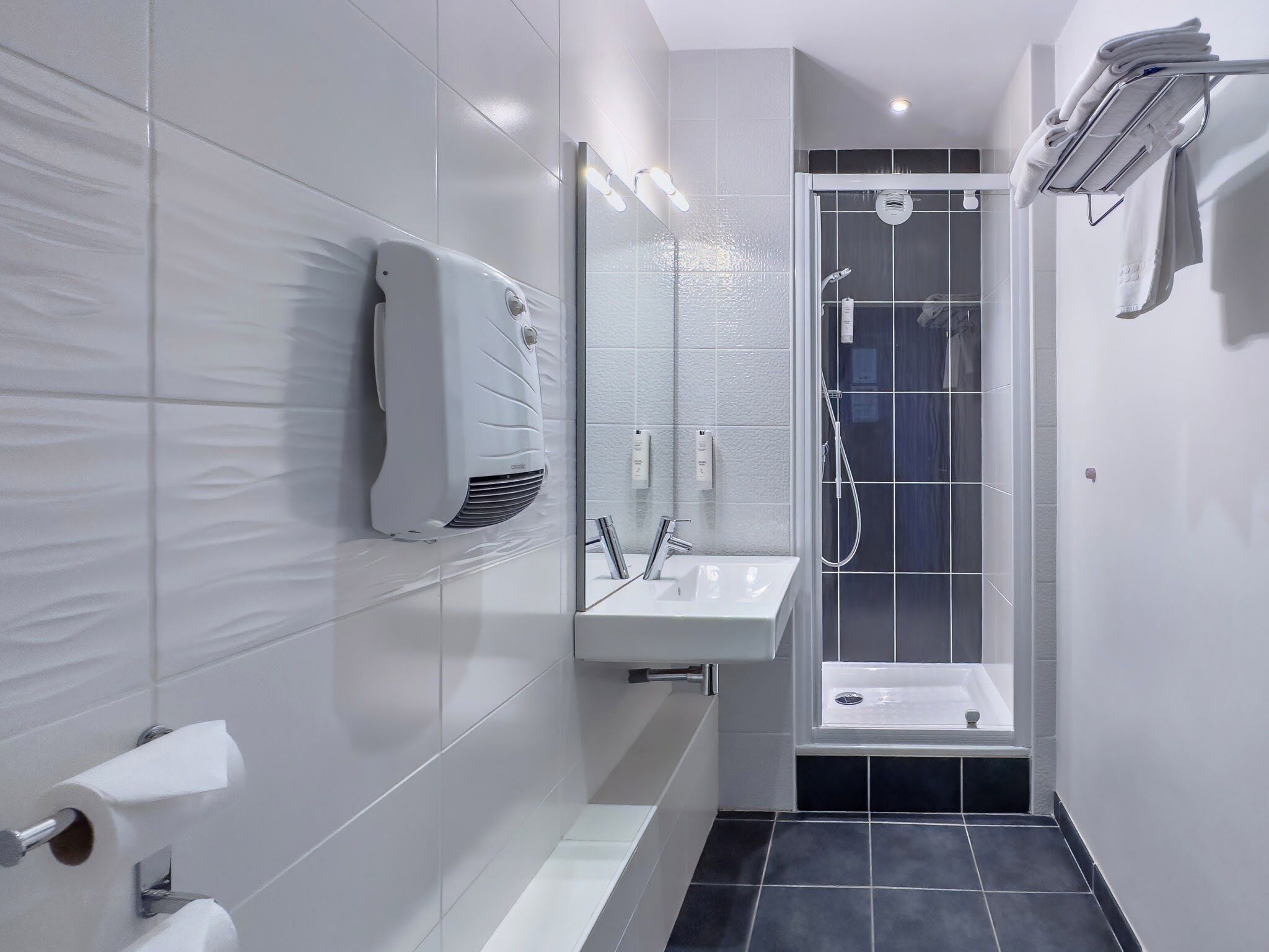 Un baño moderno con un lavabo blanco, un espejo, un perchero para toallas y una ducha.
