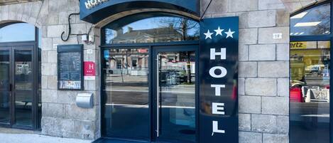 A hotel entrance with a sign reading "HOTEL DE LA GARE" and a glass door.