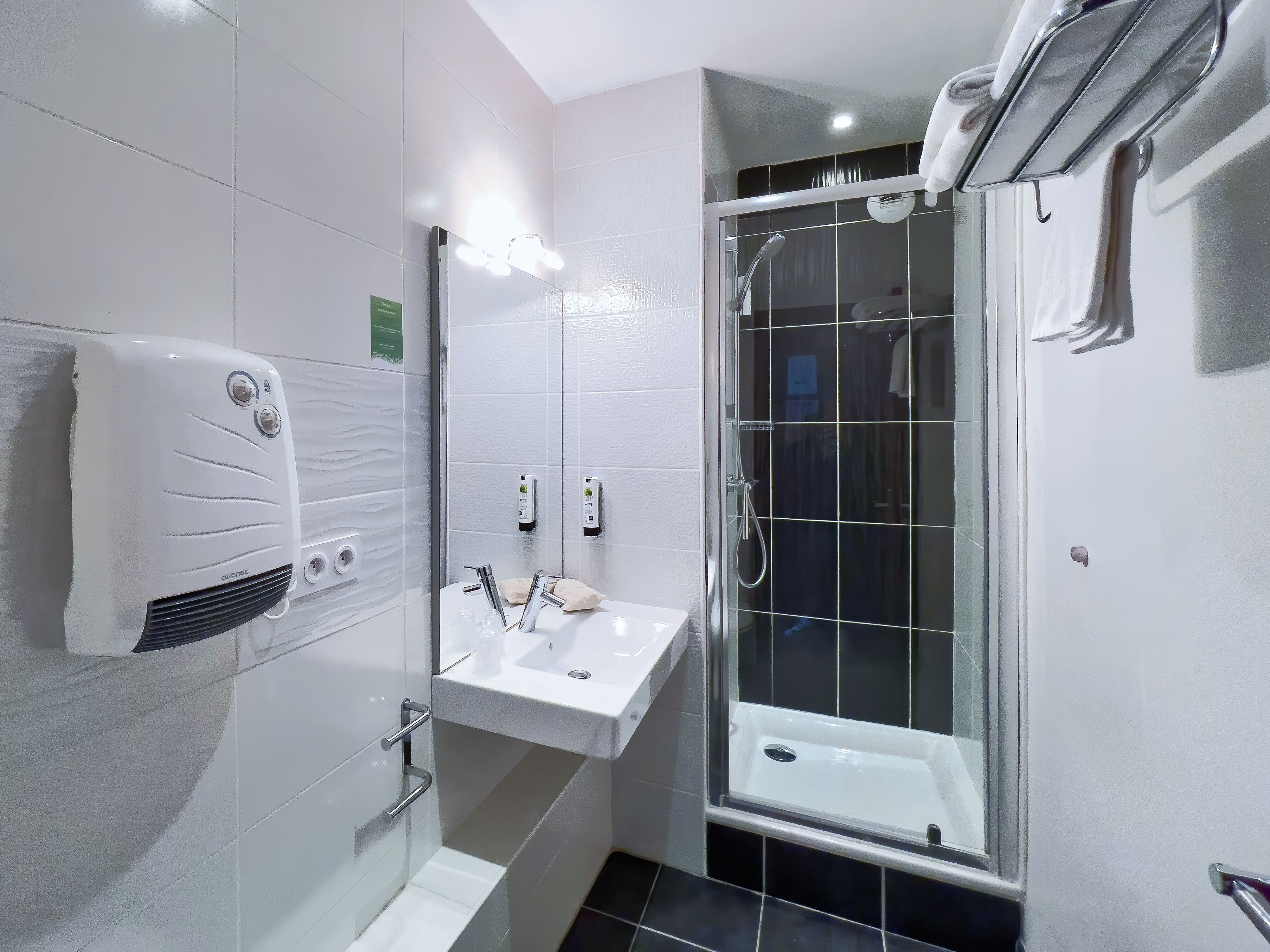 Een moderne badkamer met een wit wastafel, een douche met glazen wanden en een handdoekdispenser.