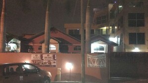 Ein Gebäude mit einem 'NOW OPEN' Schild, einer Palme und einem parkenden Auto.