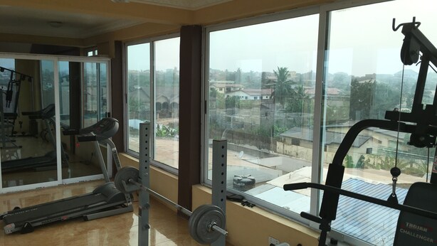 Ein Fitnessstudio mit Trainingsgeräten, großen Fenstern und Blick auf Gebäude und Bäume.