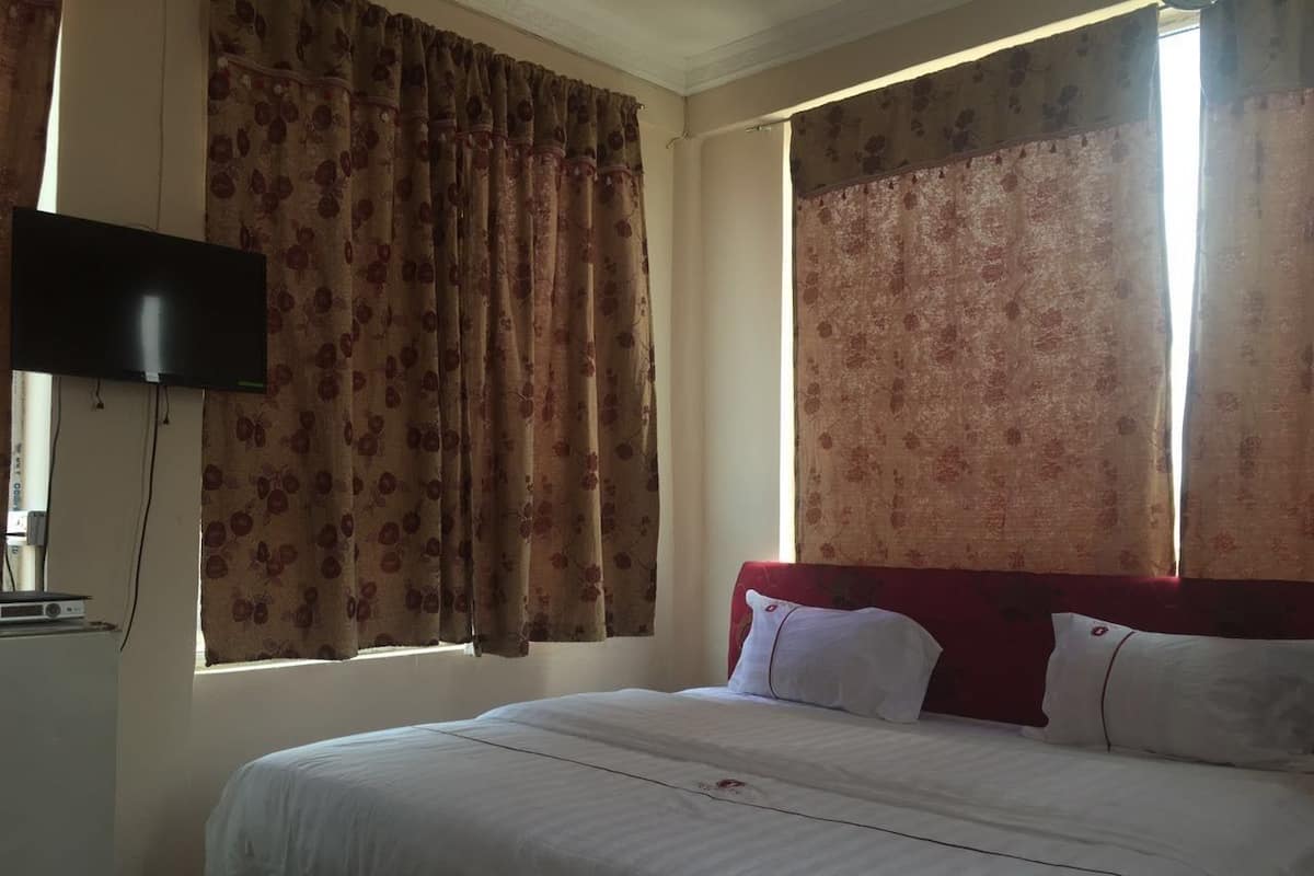 A hotel room with a bed, red headboard, floral curtains, and a flat-screen TV mounted on the wall.