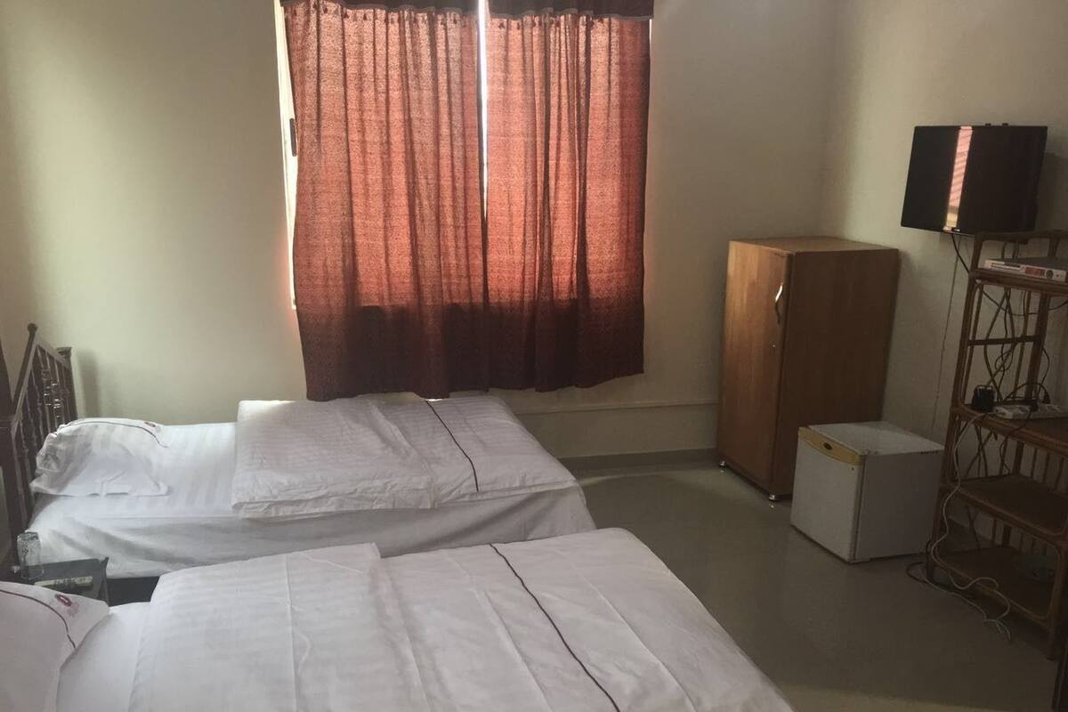A hotel room with two single beds, a wardrobe, a television, and a small refrigerator.