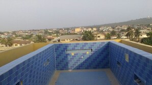 Ein Dachpool mit blauen Fliesen, umgeben von einer gelben Mauer, mit Blick auf ein Wohngebiet mit Häusern und einem Hügel im Hintergrund.