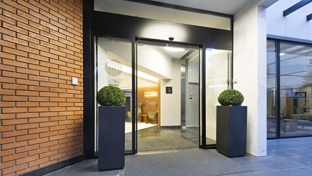 A modern building entrance with glass doors, a brick wall, and two potted plants. - Orasac Garni (Belgrade)