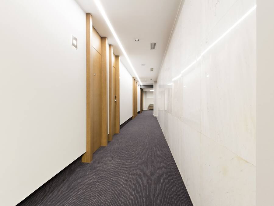 A long, narrow hallway with wooden doors on one side and white walls on the other.