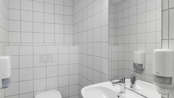 Un baño moderno con azulejos blancos, un inodoro, un lavamanos con espejo y un secamanos.