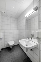 Un baño moderno con azulejos blancos, un inodoro, un lavamanos con espejo y un secamanos.