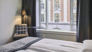 Habitación de hotel con cama, una silla, una mesa y ventana con vista a un edificio.