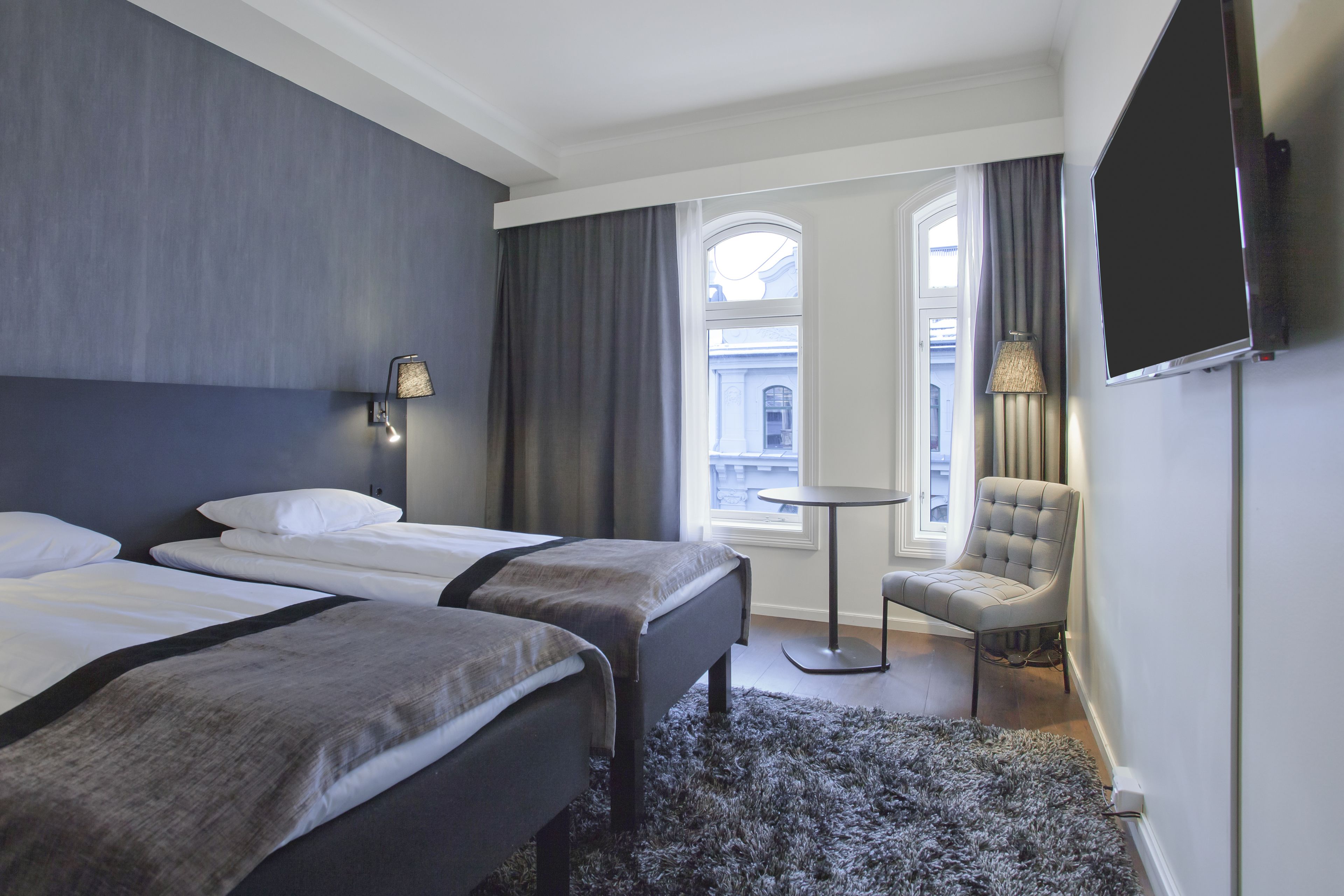 Une chambre d’hôtel avec deux lits, une petite table ronde, une chaise, un téléviseur et une fenêtre avec des rideaux.