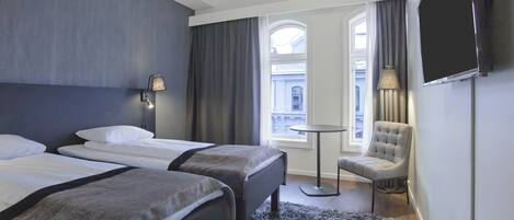 Une chambre d’hôtel avec deux lits, une petite table ronde, une chaise, un téléviseur et une fenêtre avec des rideaux.