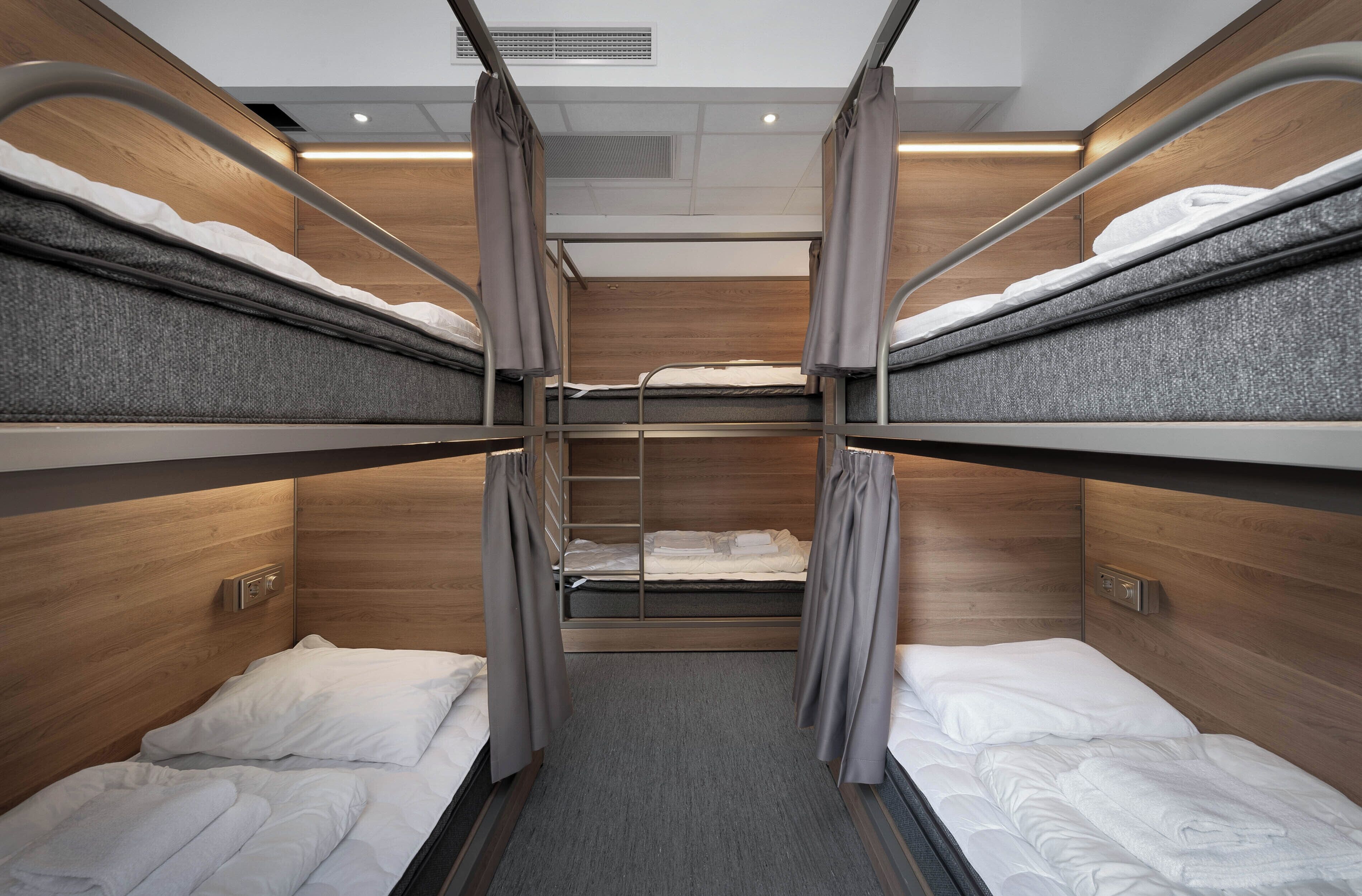 Habitación con literas, paredes de madera, alfombra gris y cortinas en las camas.