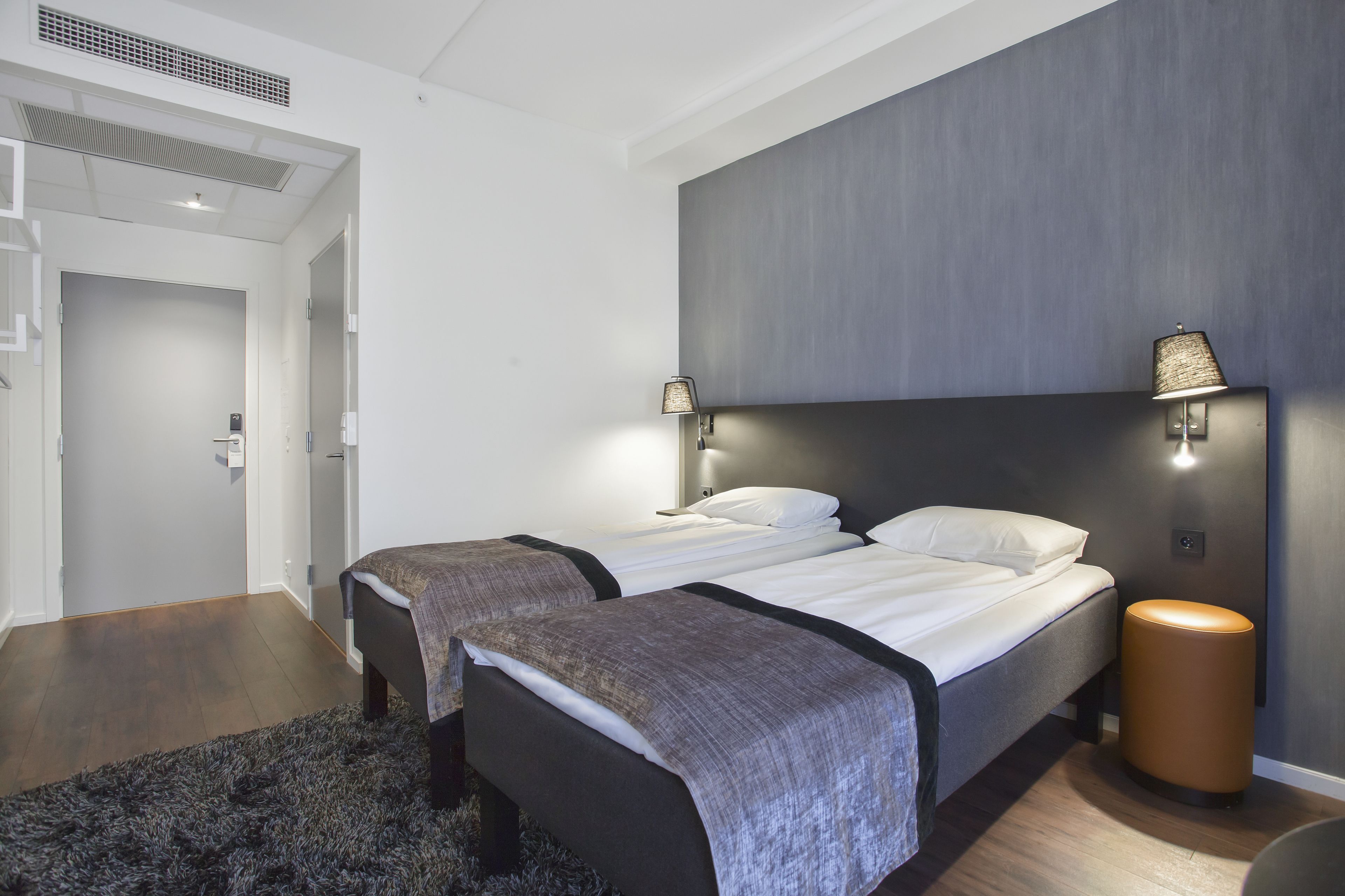 A modern hotel room with two beds, a dark headboard, a round side table, and a small rug.