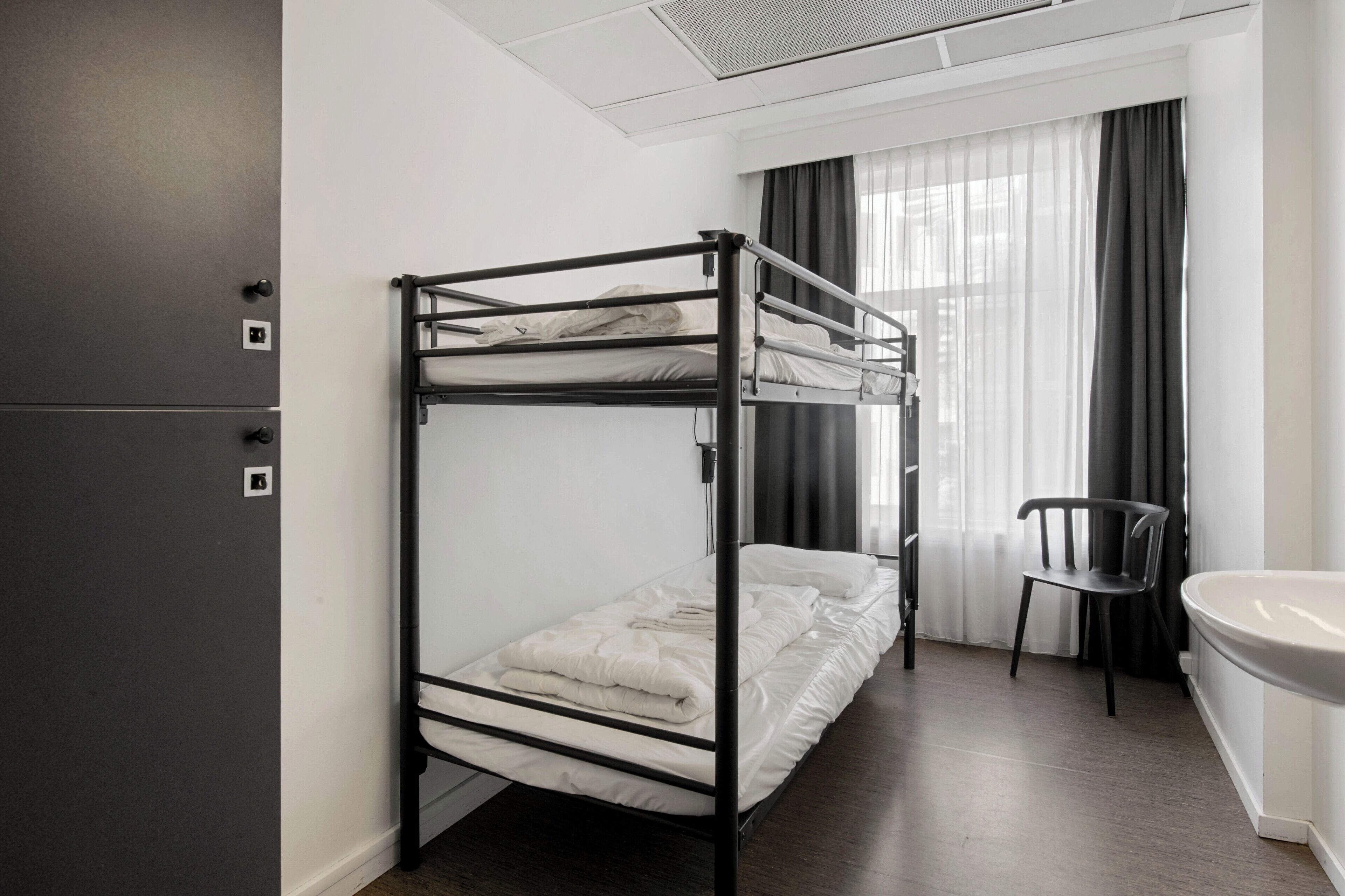 Dormitorio con literas, una ventana, una silla y un lavamanos.