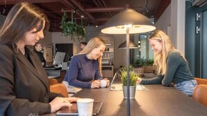 Un espacio de oficina moderno con una mesa larga, computadoras portátiles y una taza de café.