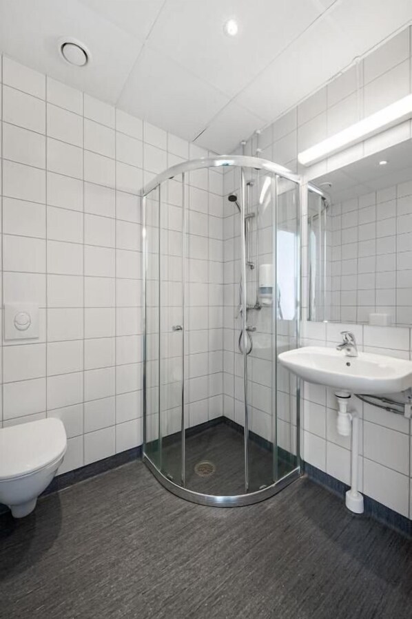 A modern bathroom with a glass-enclosed shower, a white toilet, and a sink with a mirror. - K7 Hotel Oslo (Oslo)