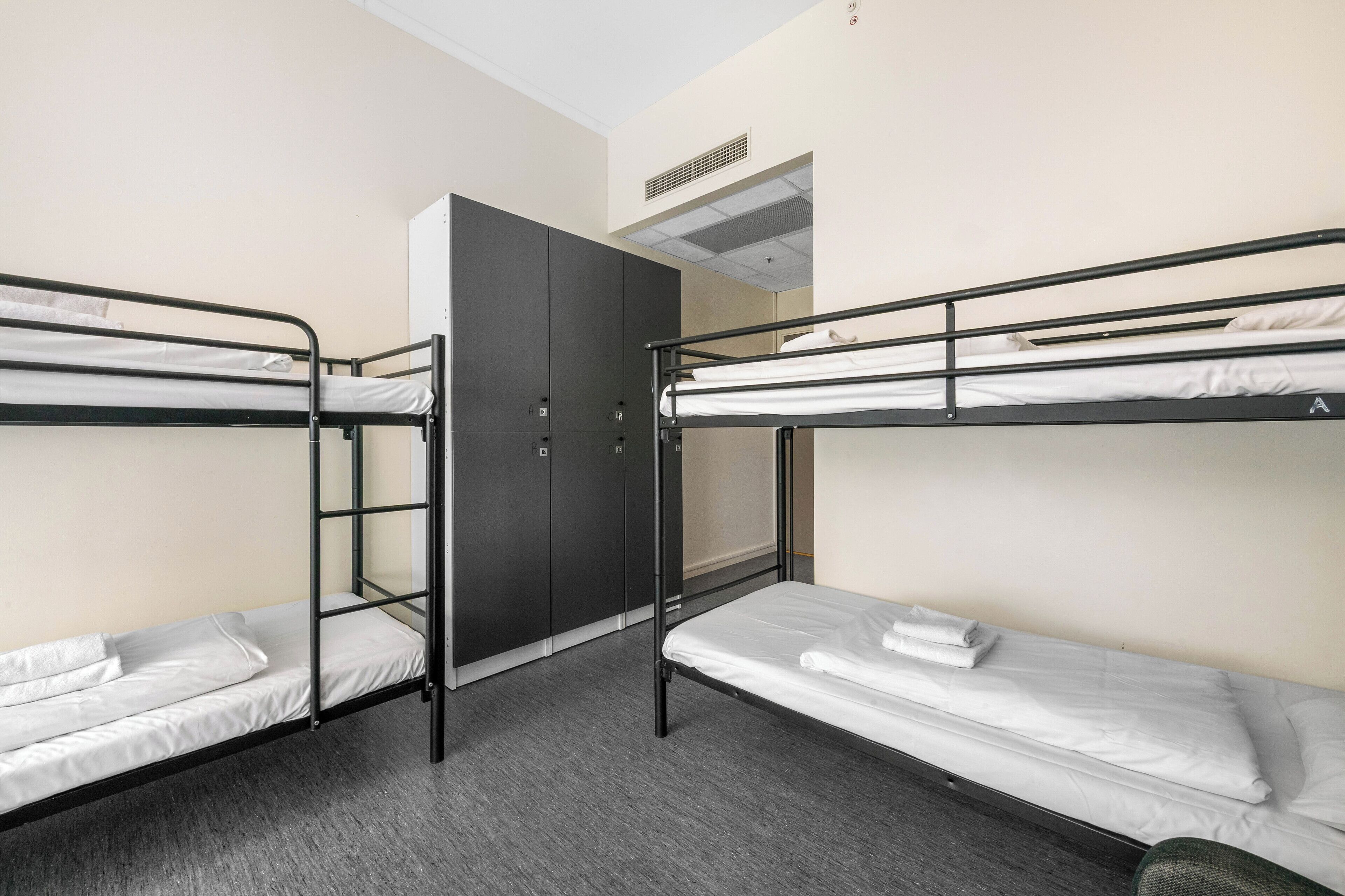 A dormitory room with bunk beds, a wardrobe, and a ventilation system.