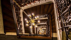 Un candelabro con varias bombillas colgando de una estructura metálica, una ventana con diseño decorativo y un techo de madera.