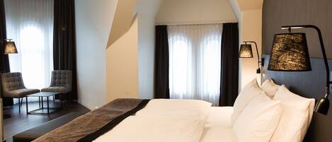 Habitación de hotel con una cama grande, dos lámparas de noche, una silla y vistas al exterior a través de la ventana.