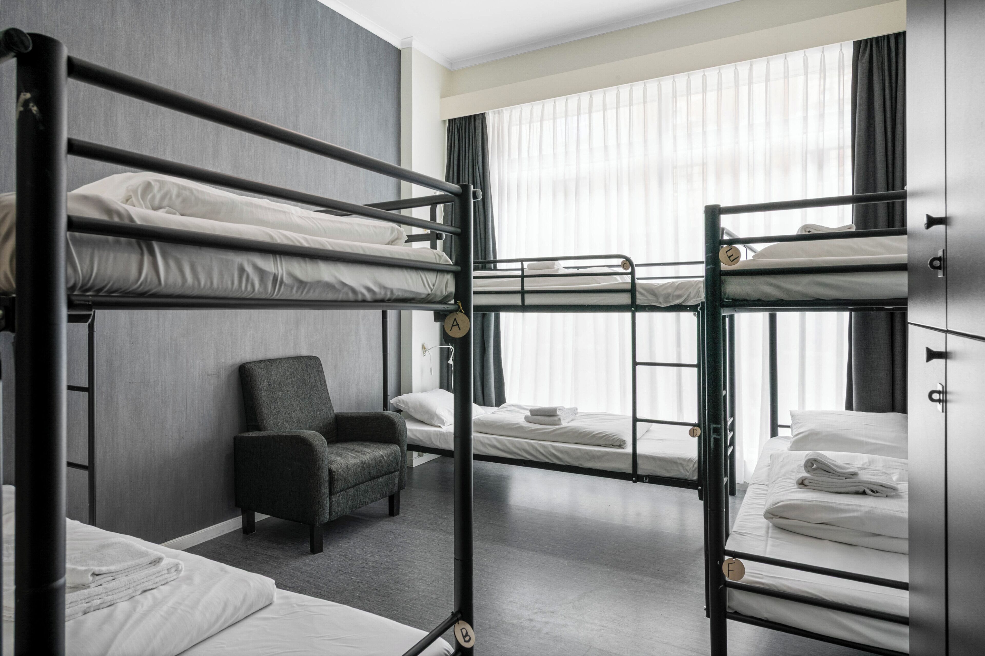 Una habitación con literas, una silla y un ventanal con cortinas.