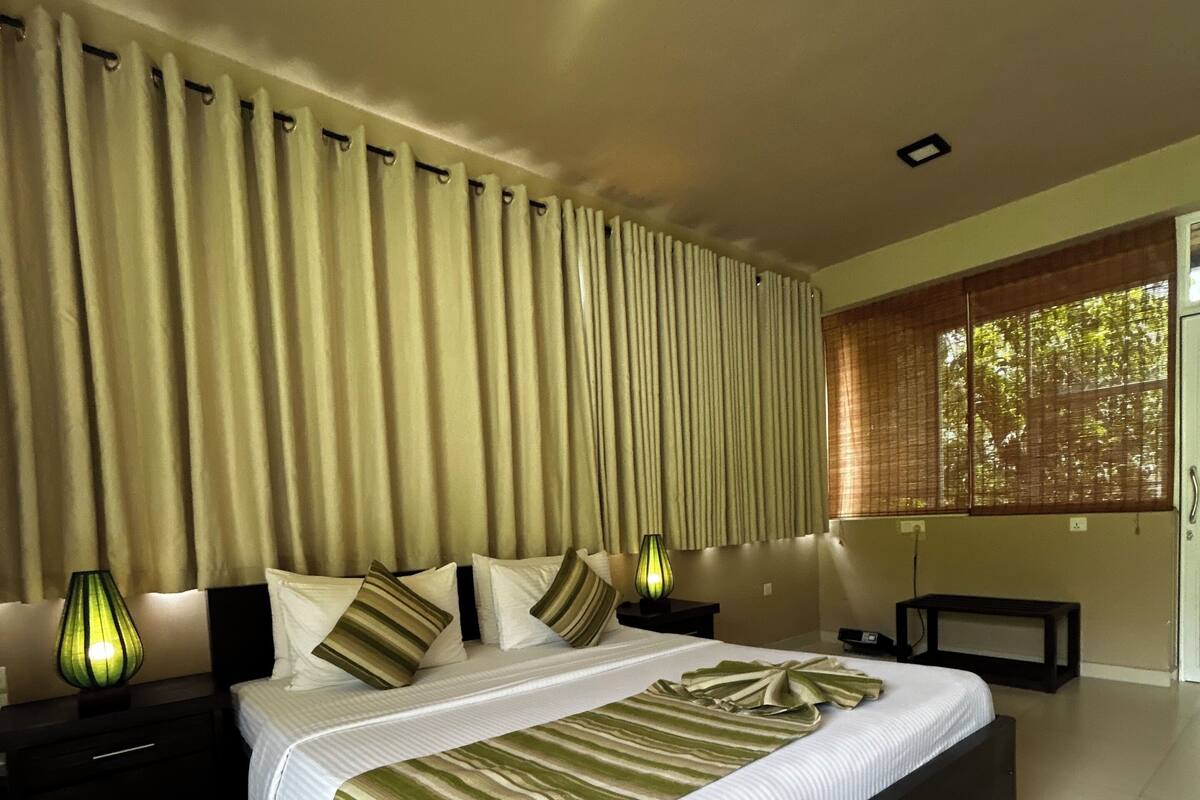 Quarto com uma cama grande, mesa de cabeceira, abajur e janela com persianas.