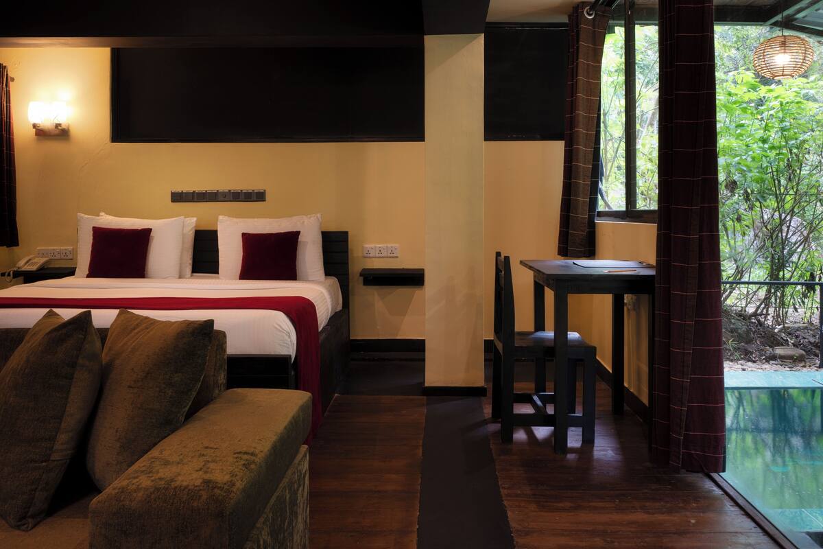 Quarto de hotel com cama, sofá, mesa de jantar e vista para o verde lá fora.